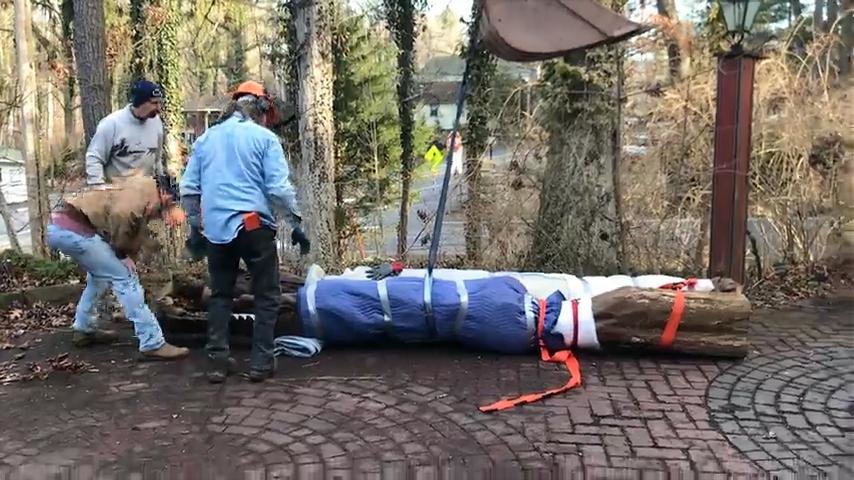 Two workers carefully handling a bundled carving laid on its side on a brick patio during removal from its original location