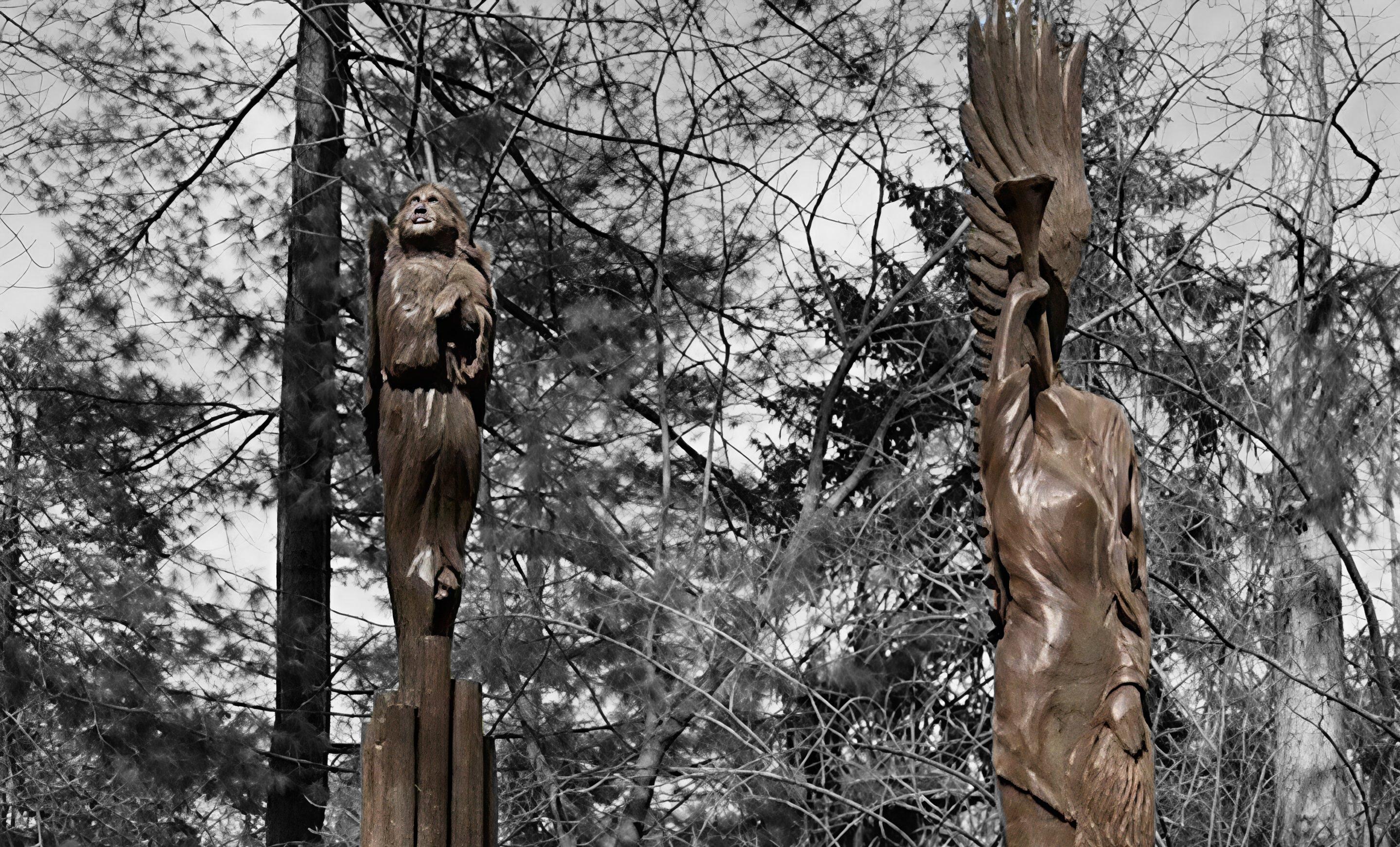 Two tall wood-carved sculptures — Archangel Gabriel and The King of Instruments — standing amid bare winter trees